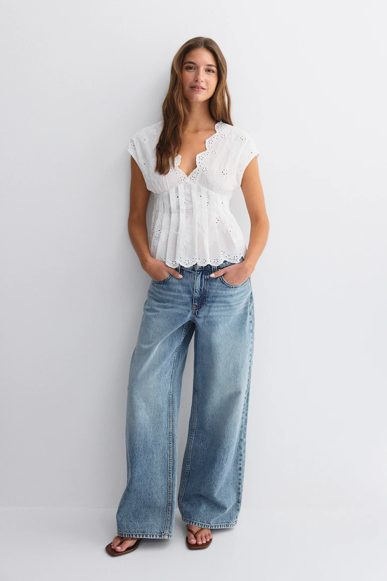Vit broderie anglaise-blus i öljett med skulpterad V-ringning, cap-ärmar och veckad peplummidja; ljusblå jeans med hög midja och vida ben; bruna sandaler med fyrkantig tå.