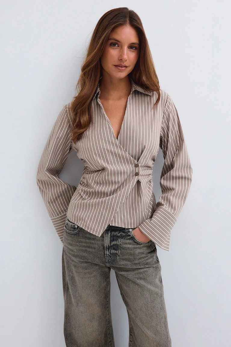 Beige striped wrap blouse with a pointed collar and flared sleeves, paired with faded grey jeans.