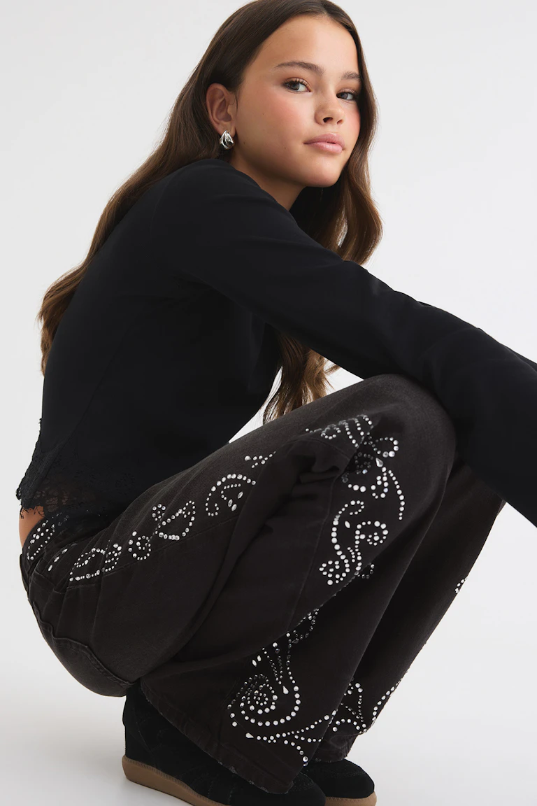 Black long-sleeve top with lace trim, black embellished wide-leg trousers, and black shoes.
