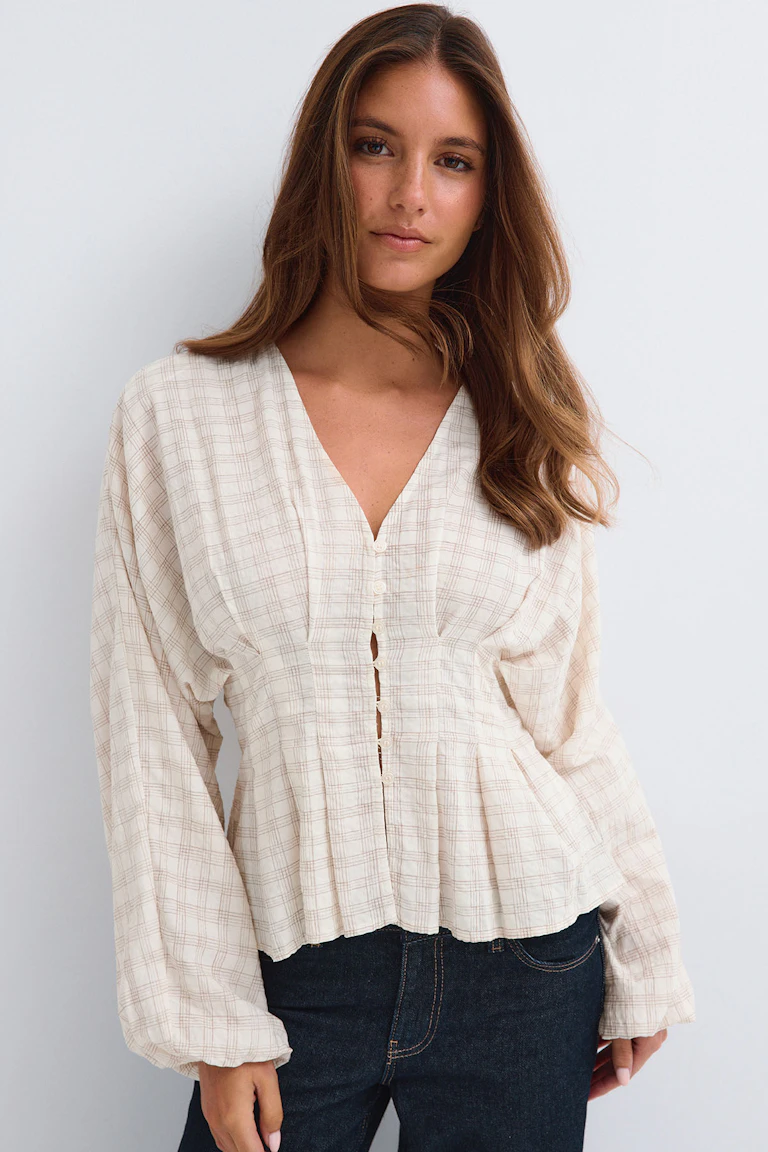 Cremefarvet bluse med ternet mønster og knapper foran samt lange, voluminøse ærmer, kombineret med mørke jeans.