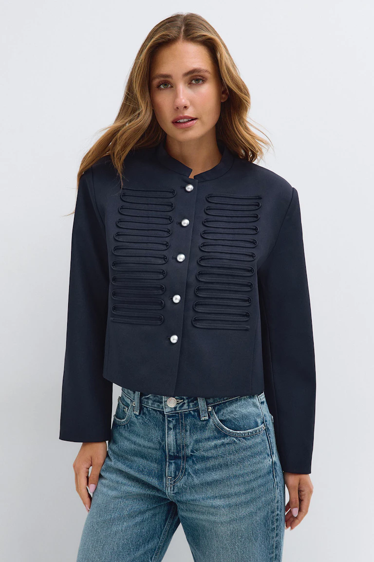 En marineblå skræddersyet jakke med dekorative snore og sølvknapper, kombineret med lyseblå jeans.