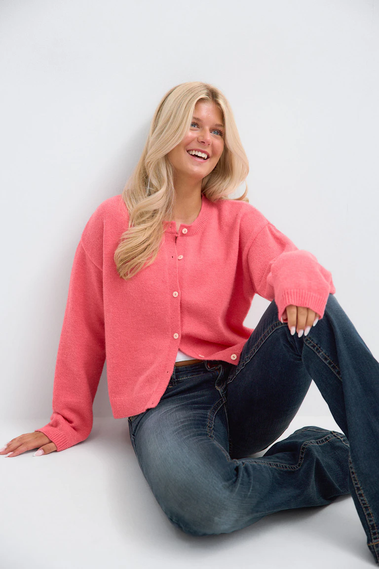 Korallrosa cardigan med knappefront og ribbestrikkede mansjetter og nederkant, båret over en matchende rosa blondekamisole, sammen med en lettvasket, slitt denimshorts med frynsete nederkant.