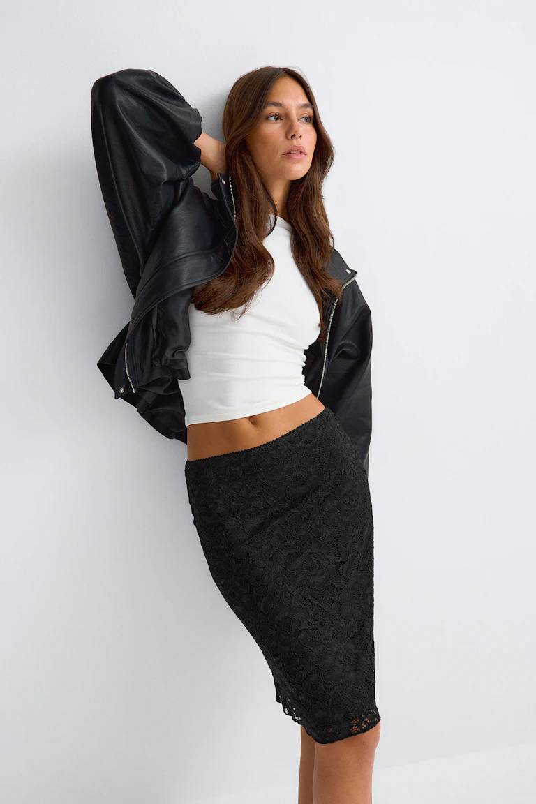 Schwarze Lederjacke, weißes Crop-Top und schwarzer Midirock aus Spitze.