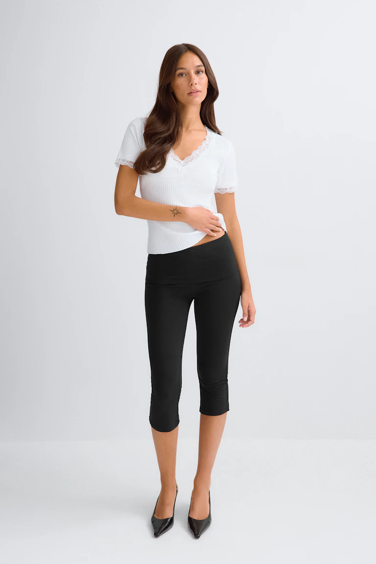 Vit topp med V-ringning och spetskant tillsammans med svarta capri-leggings.