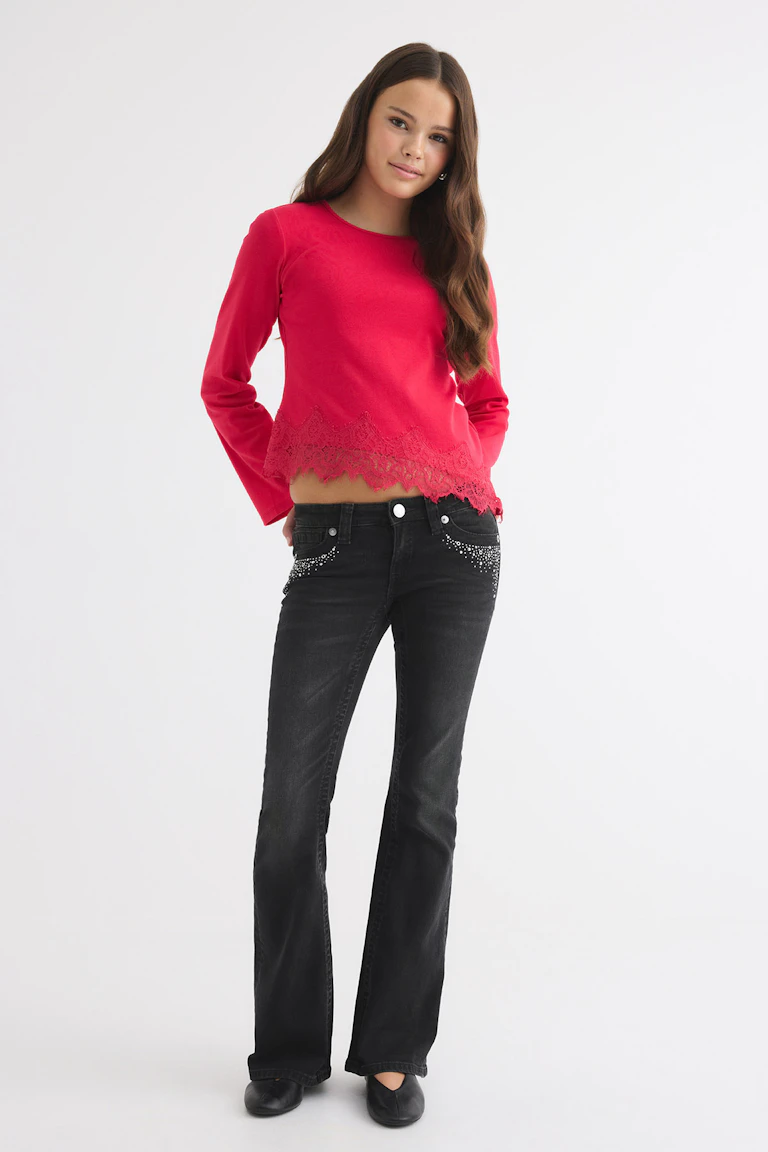 Bright pink long-sleeve top with a lace hem, paired with black flared jeans and black flats.