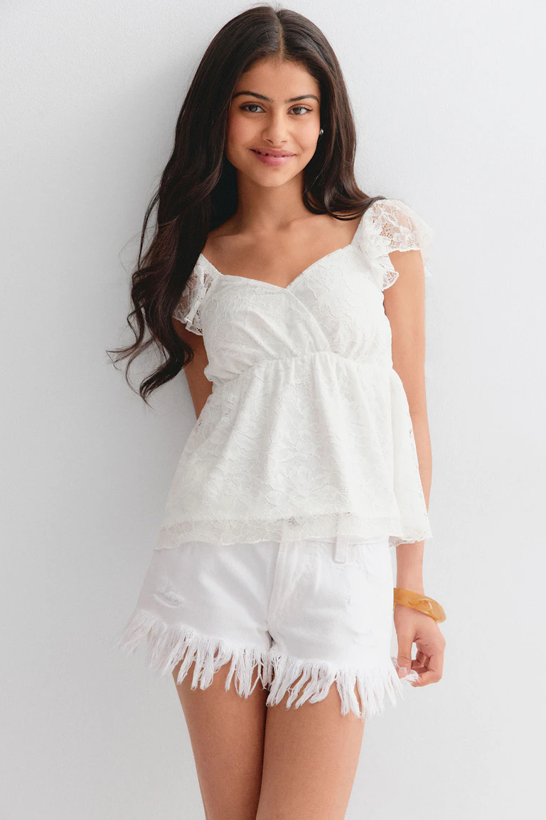 Peplumtop i hvid blonde med hætte og hjerteudskæring, sat sammen med hvide distressed denimshorts med flosset kant og et ravfarvet armbånd.