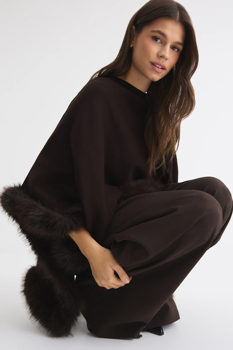 Donkerbruine oversized set met een broek met wijde pijpen, met bont afgezette broekspijpen en zoom, en zwarte hakken.