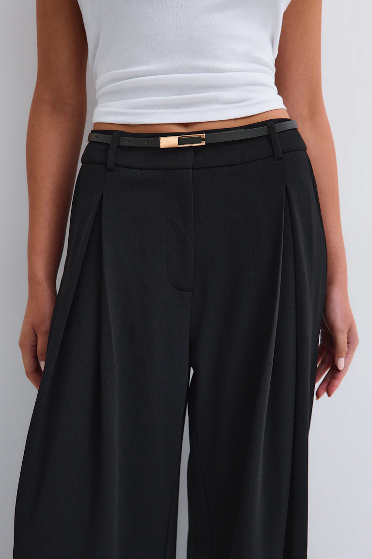 Un haut blanc sans manches, associé à un pantalon noir à taille haute et à jambes larges, ainsi qu'à une ceinture noire fine dotée d'une boucle dorée.