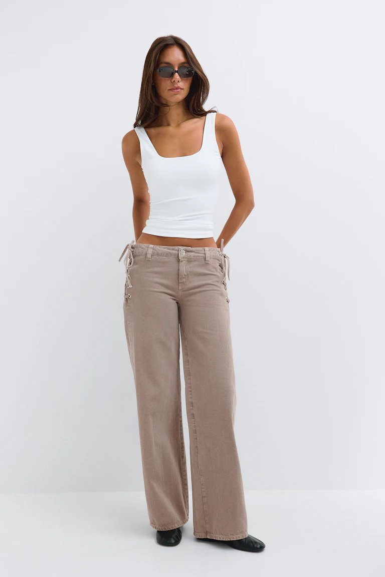 White square-neck tank top with beige wide-leg lace-up trousers and black flats.