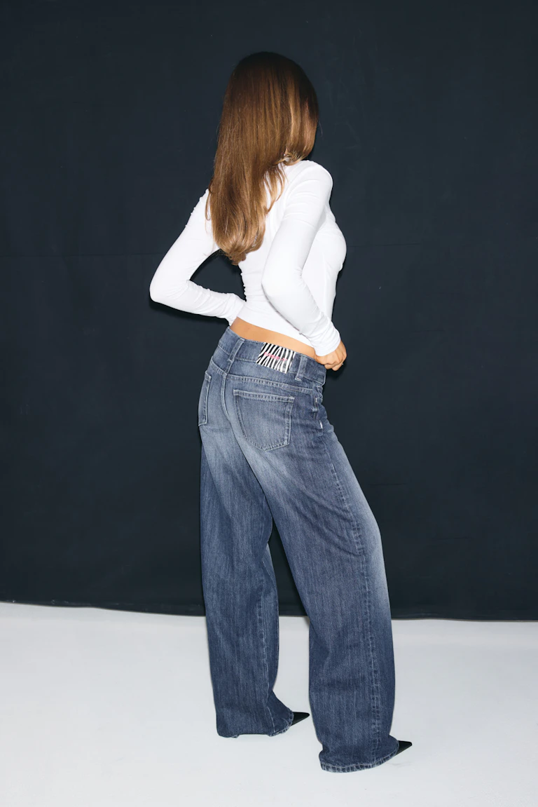 Fitted white long-sleeve top with wide-leg blue jeans.