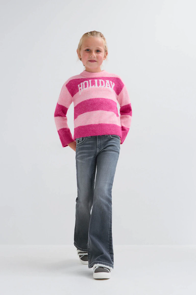 Ein rosa-magenta gestreifter Pullover mit der Aufschrift „Holiday“, eine dunkle Jeans mit ausgestelltem Bein und graue Sneaker.