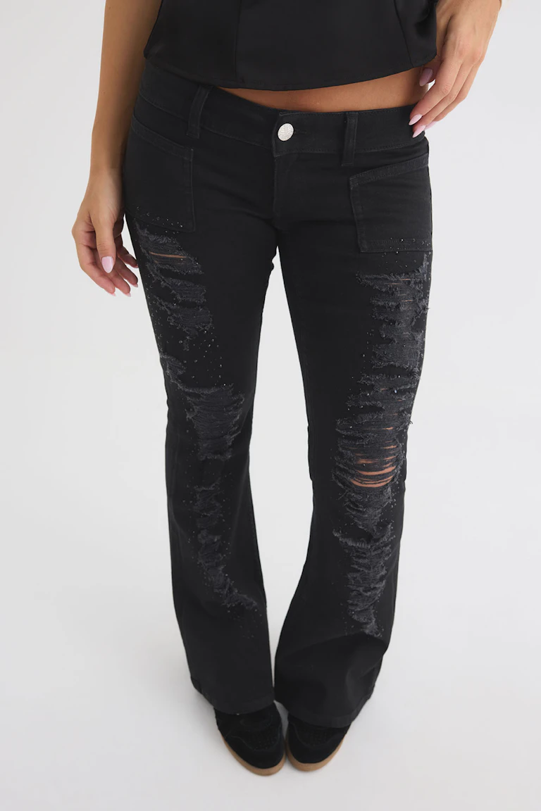 Schwarzes bauchfreies Top zu einer schwarzen, hoch taillierten Jeans im Used-Look mit ausgestelltem Bein.