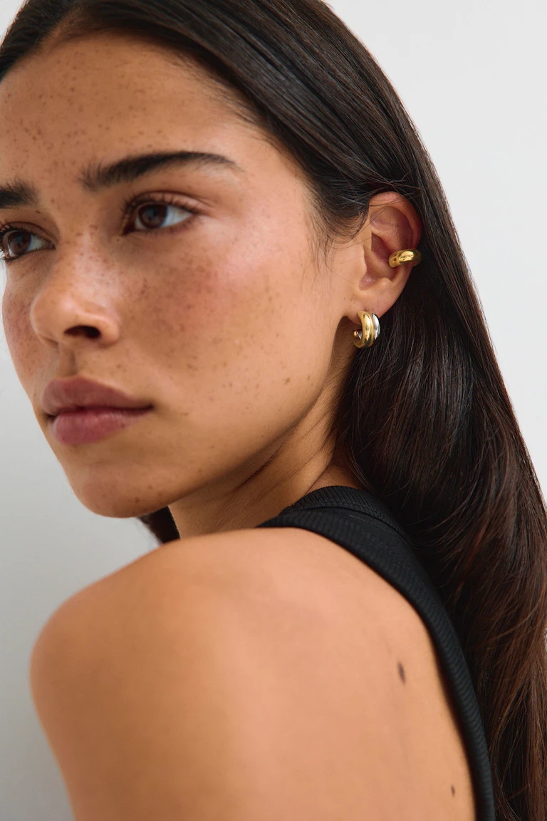 Black sleeveless top with gold hoop earrings.