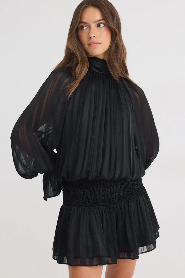 Schwarze, transparente Bluse mit hohem Kragen und voluminösen Ärmeln, kombiniert mit einem schwarzen Minirock mit Rüschen.