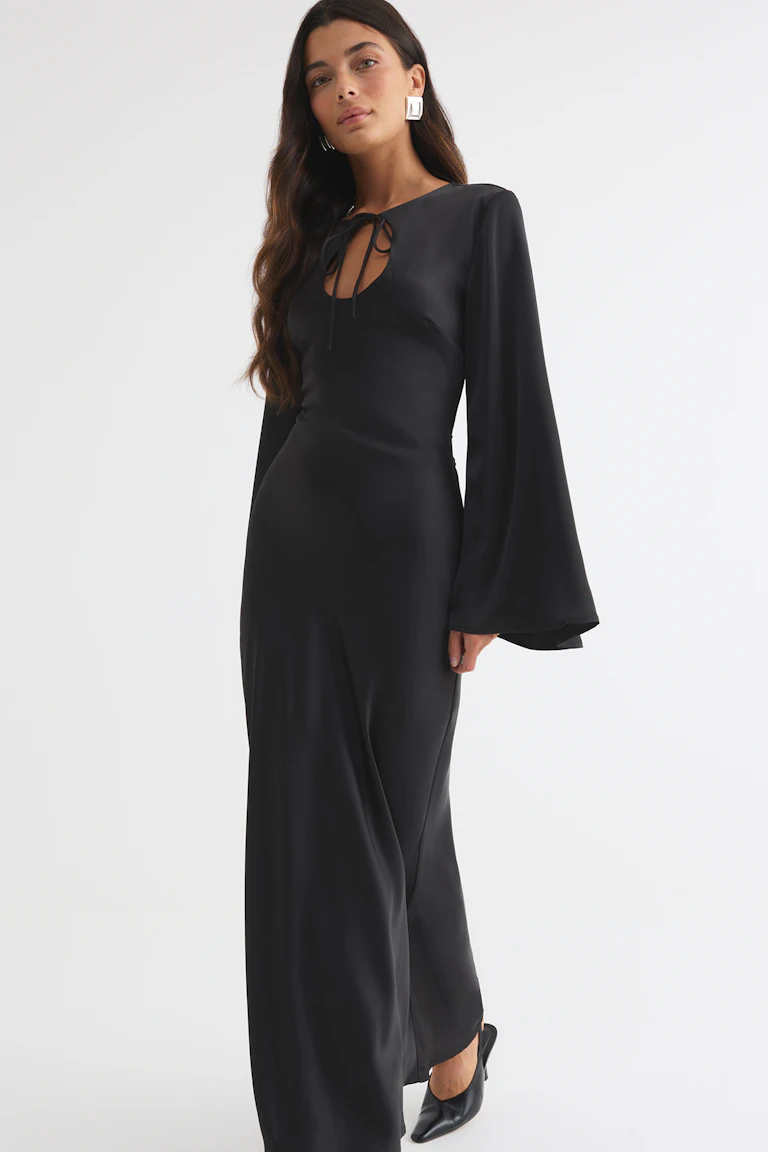Black floor-length dress with a tie-front keyhole neckline, long flared sleeves, and black pointed heels.