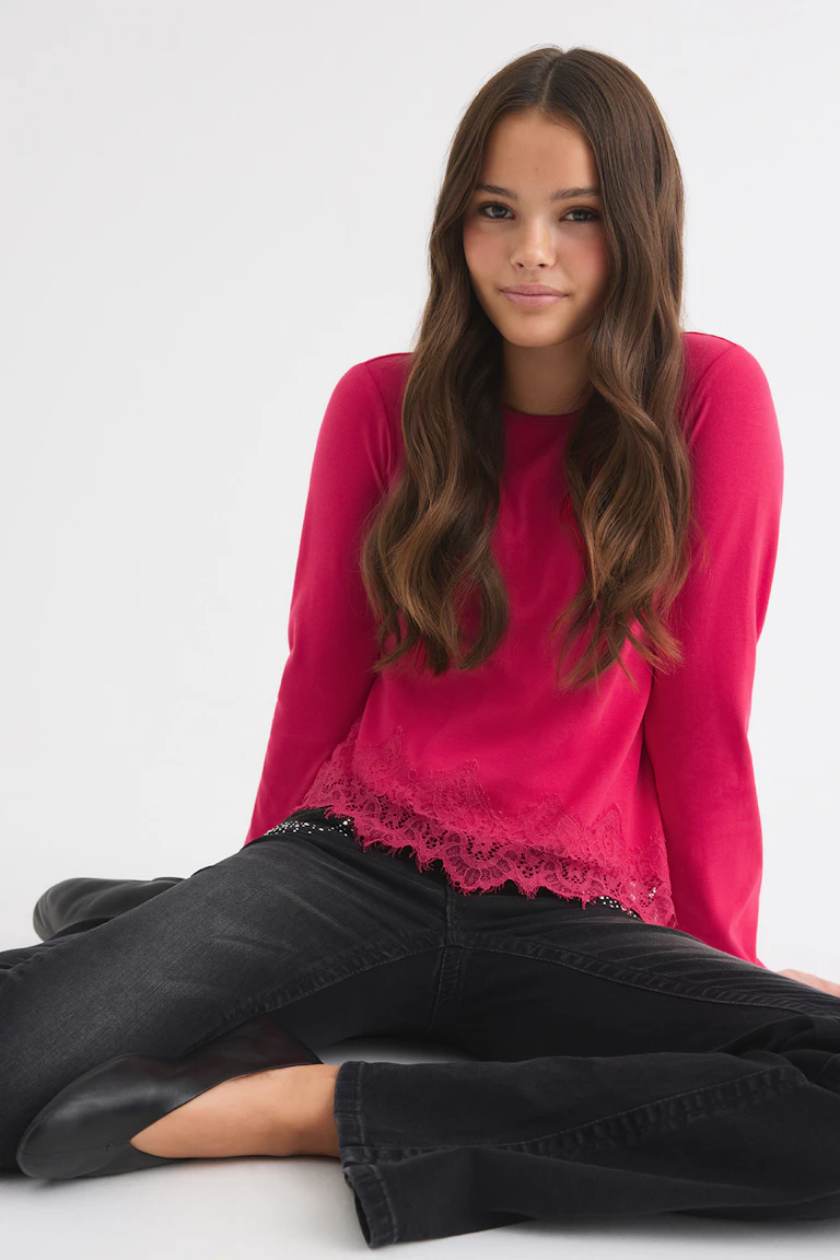 Bright pink long-sleeve top with lace trim, paired with black wide-leg jeans.