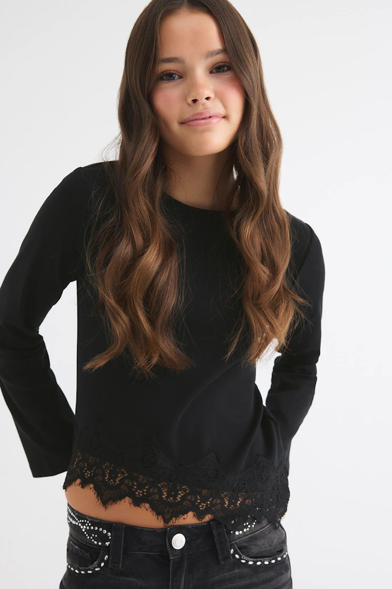 Black long-sleeve top with lace hem and black embellished jeans.