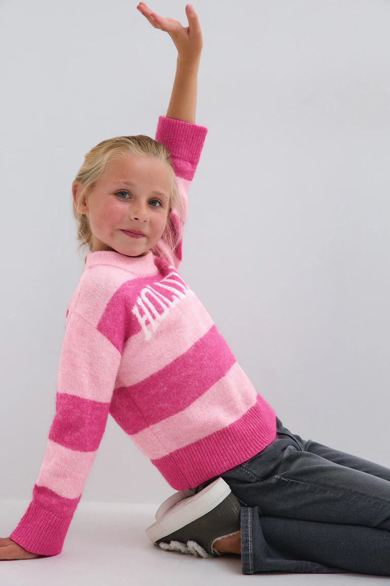 Pink and light pink striped knit sweater with dark jeans.