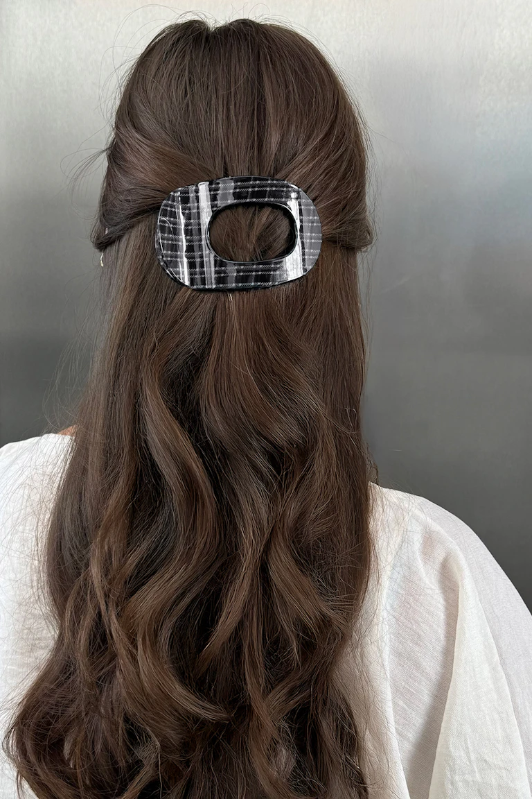 Eine schwarz-weiß karierte Haarspange, die langes, welliges braunes Haar zusammenhält, dazu ein weißes Oberteil.