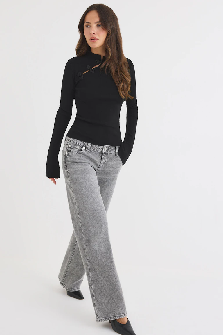 Svart långärmad topp med blommiga detaljer, grå jeans med vida ben och svarta spetsiga klackar.