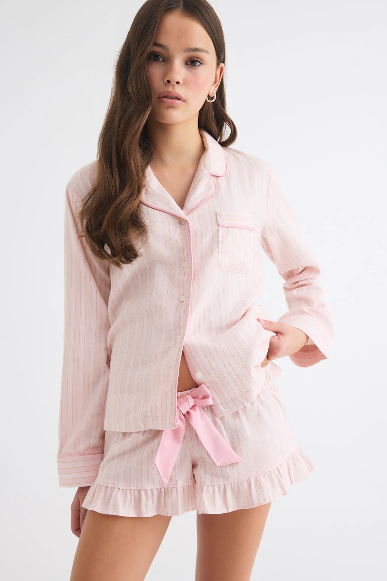 Light pink striped pajama set with a button-up long-sleeve top and ruffled shorts tied with a pink satin bow.
