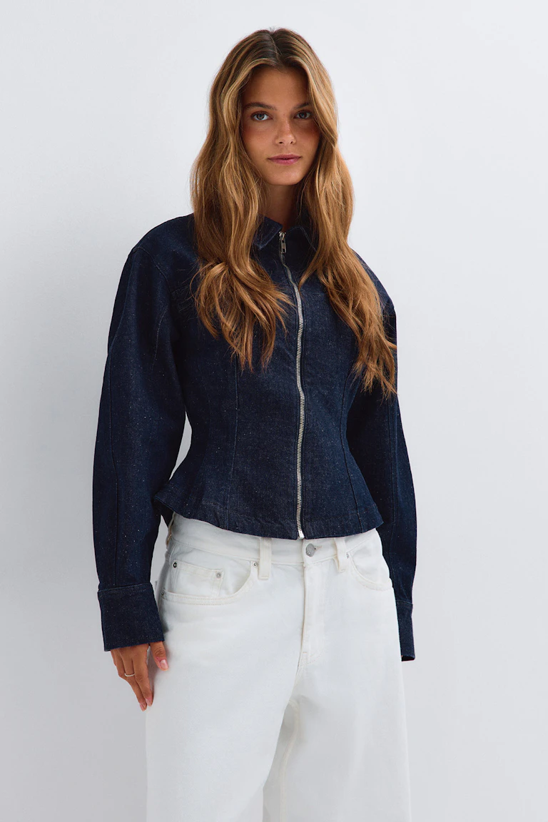 Mörk jeansjacka med dragkedja fram och vita jeans.