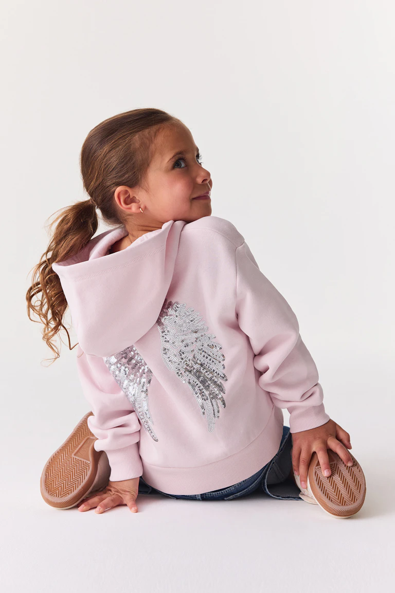 ID 343680, StyleColorSupplier 11519-E: ljusrosa tröja med huva och vinge-detalj i paljetter, i kombination med blå jeans.