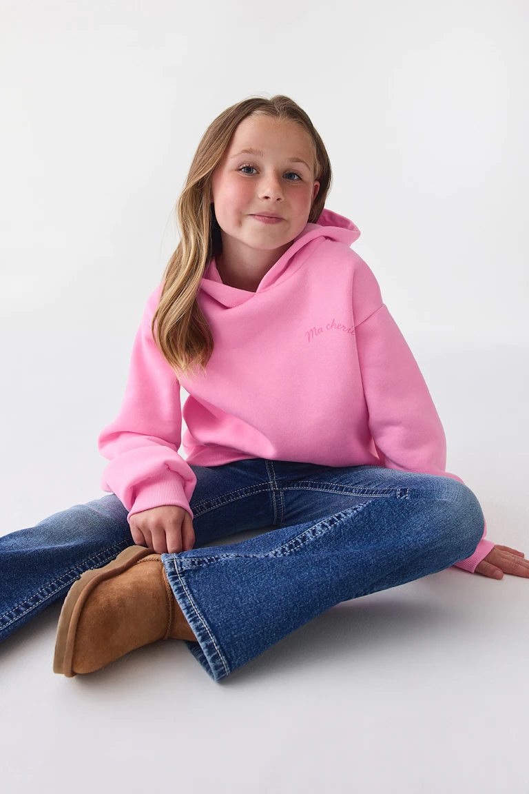 Ein hellrosa Kapuzenpullover, eine blaue Schlagjeans und braune Wildlederstiefel.