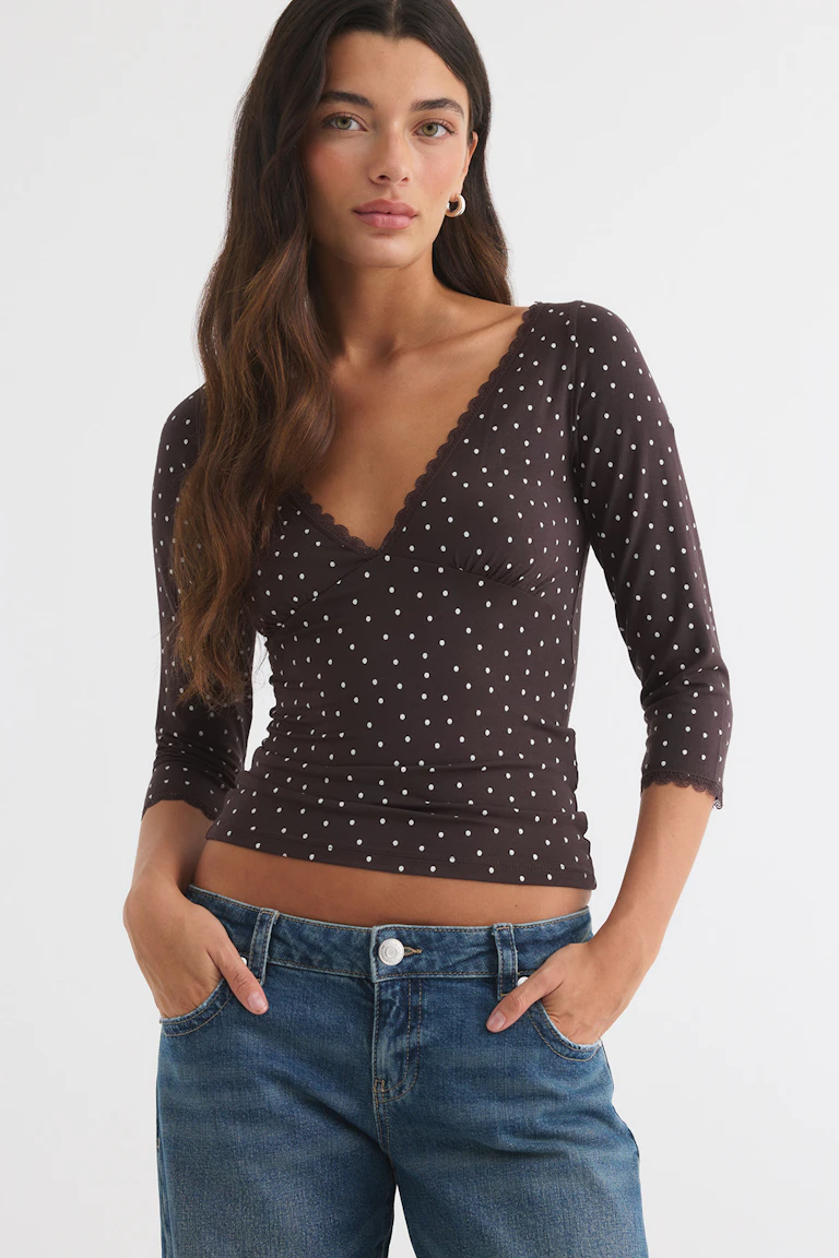Un haut marron foncé à pois, à col en V et bordé de dentelle, porté avec un jean bleu.
