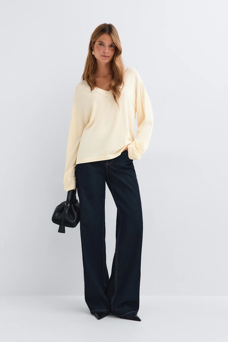 Cream V-neck sweater with relaxed sleeves, dark wide-leg jeans, black pointed-toe shoes, and a black handbag.