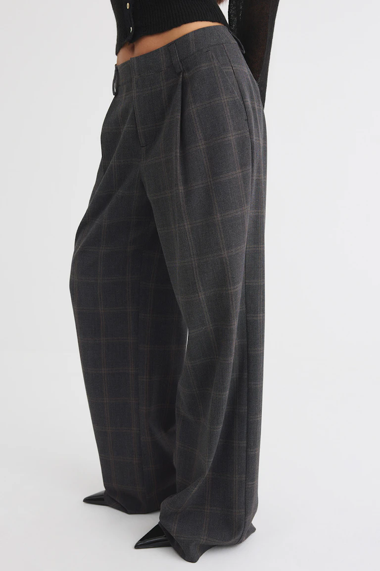 Zwarte, kort gesneden gebreide top met een donkere geruite broek met wijde pijpen.