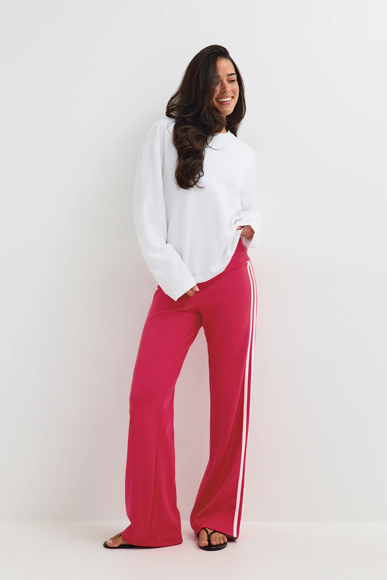 White oversized long-sleeve top, bright pink wide-leg trousers with white side stripes, and black flat sandals.