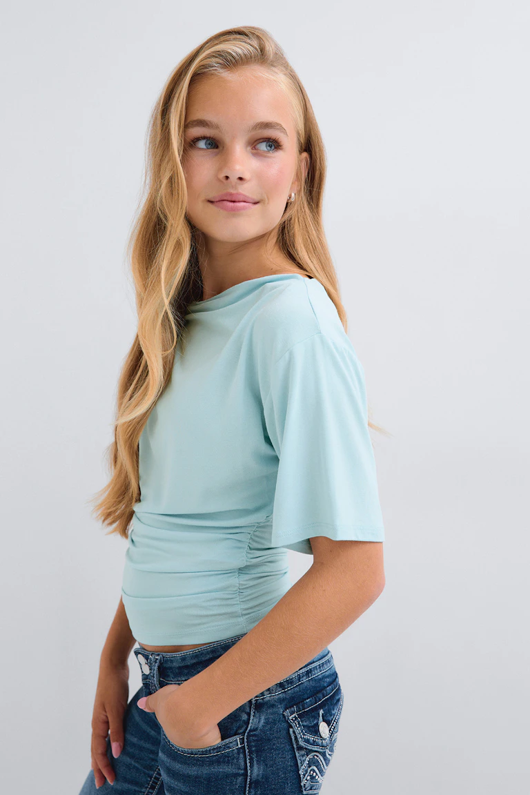 Hellblaues, kurzärmeliges, gerafftes Oberteil zu blauen Jeans.