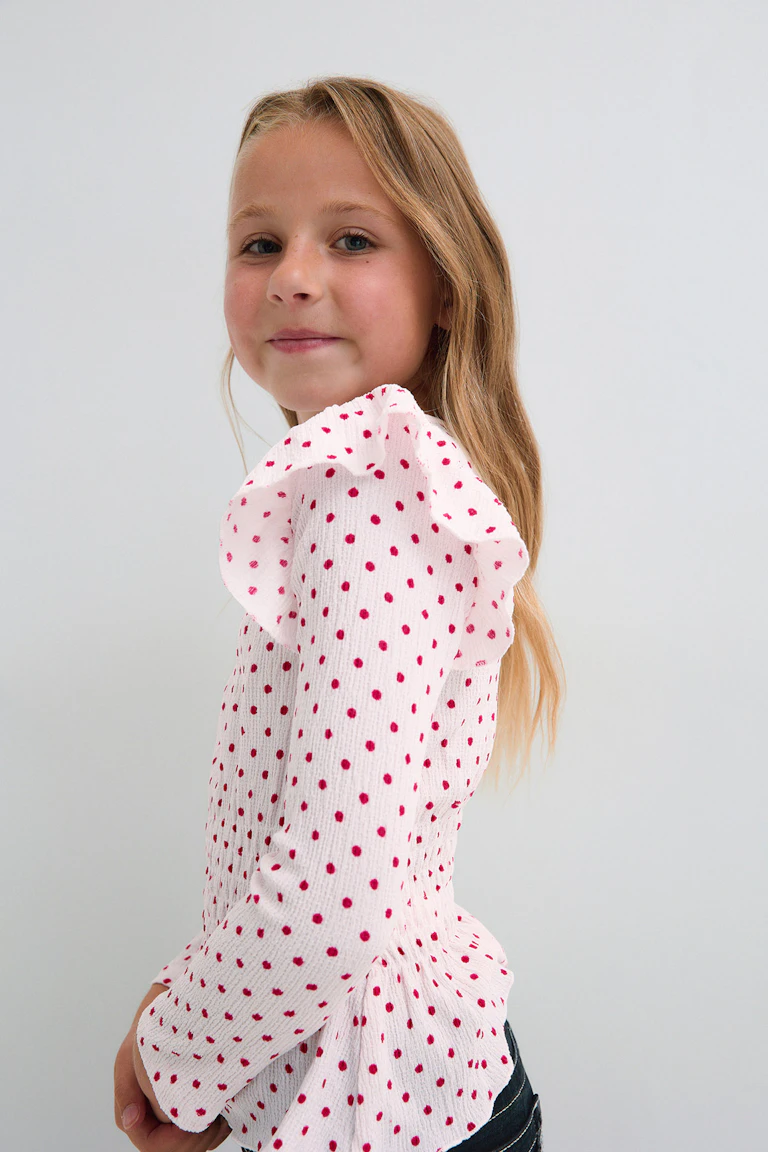 Weiße Langarmbluse mit rosa Punkten, Puffärmeln und dunkler Jeans.