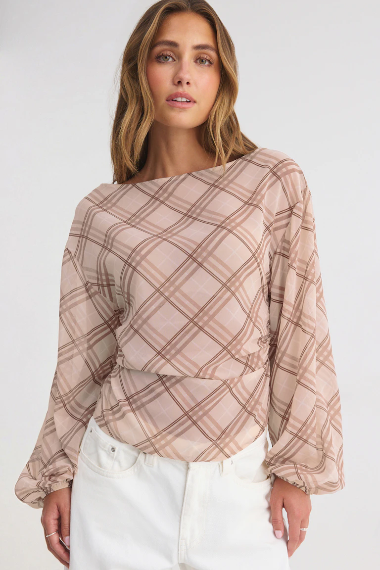 Ze draagt een roze geruite blouse met lange mouwen en een witte broek.