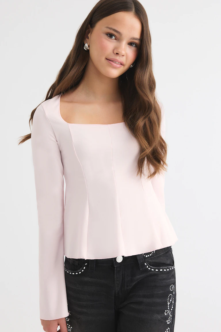Hellrosa Langarm-Oberteil mit quadratischem Ausschnitt, kombiniert mit einer schwarzen Jeans mit Strassverzierung.